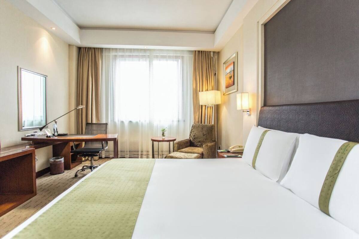 A hotel room with a bed, desk, chair, lamp, and curtains.