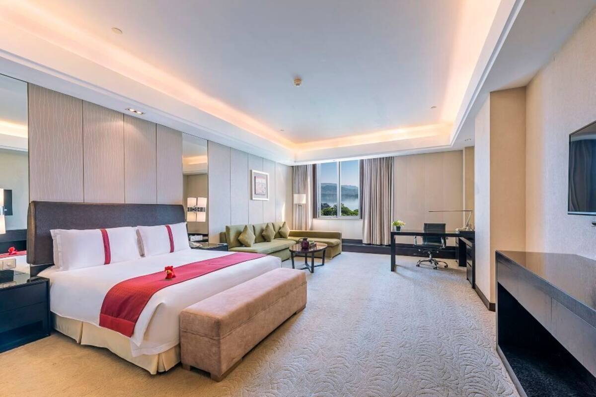 A hotel room with a large bed, a sofa, a desk, and a TV.