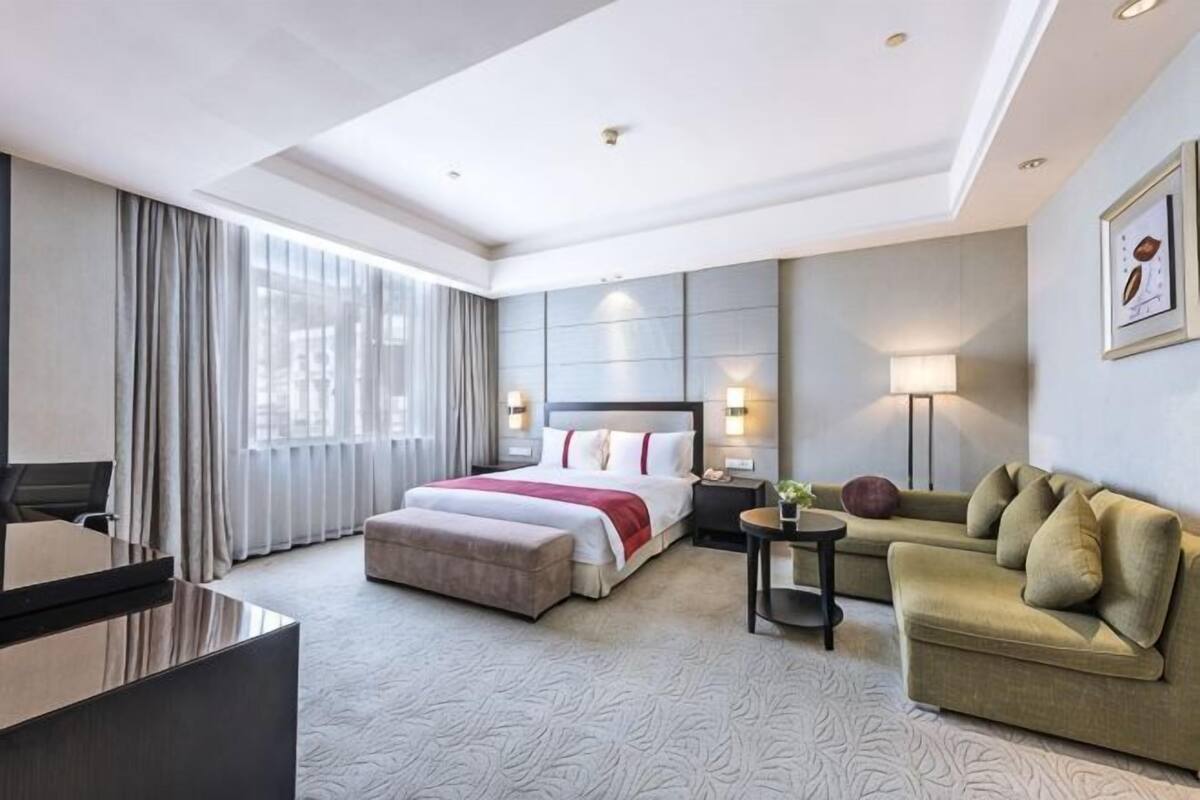 A hotel room with a bed, a sofa, a desk, and a lamp.