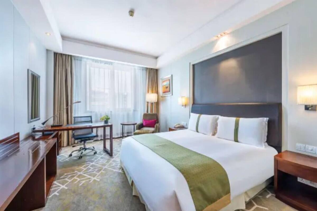 A hotel room with a large bed, a desk, a chair, and a small table.