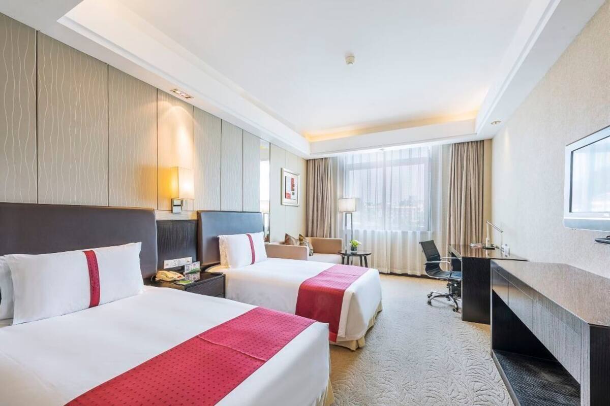 A hotel room with two beds, a desk, a chair, a TV, and a window with curtains.