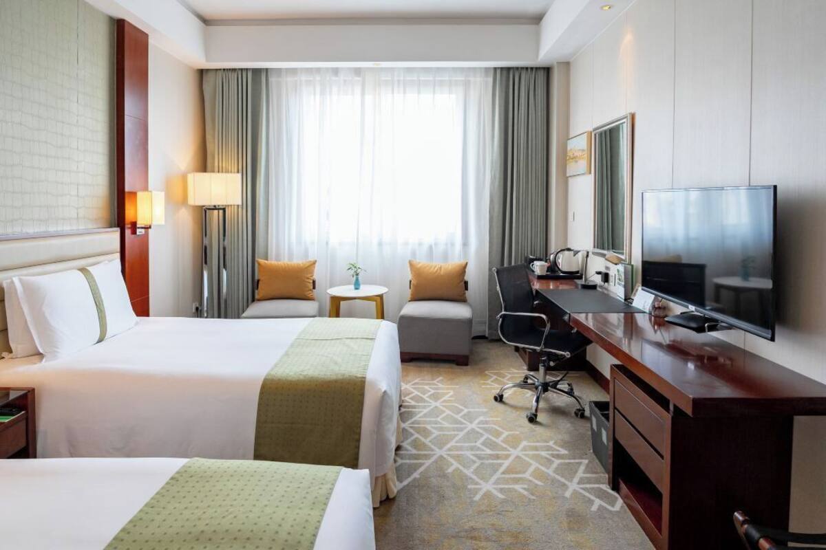 A hotel room with two beds, a desk, a chair, a TV, and a window with curtains.