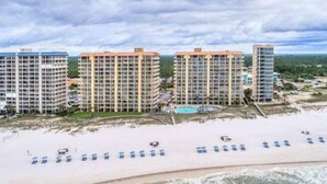 A beachfront hotel with multiple high-rise buildings, a sandy beach, and a pool area. - Summer House Beachfront Condos (Orange Beach)