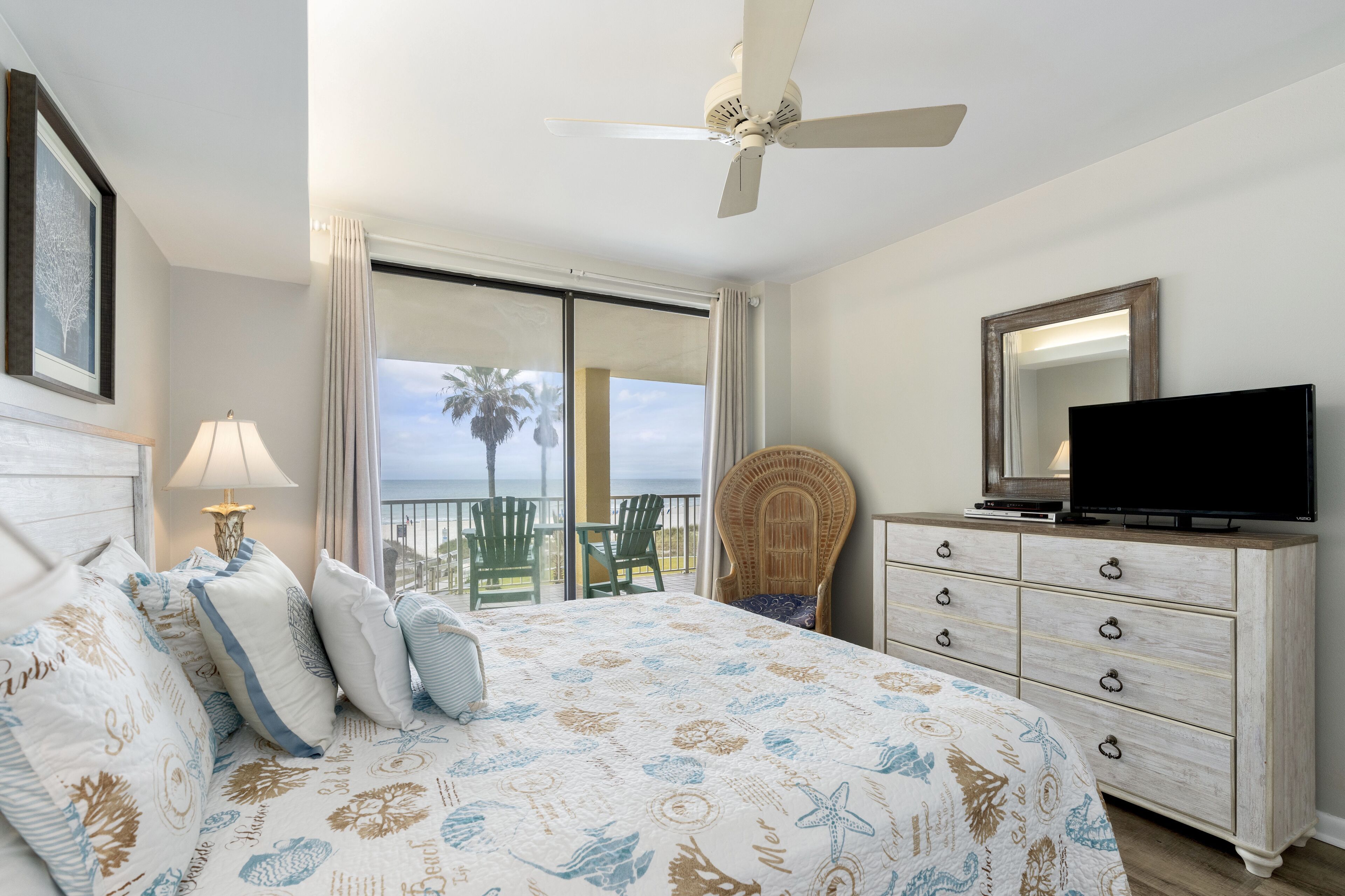 A bedroom with a bed, a dresser, a television, and a balcony with a view of the ocean.