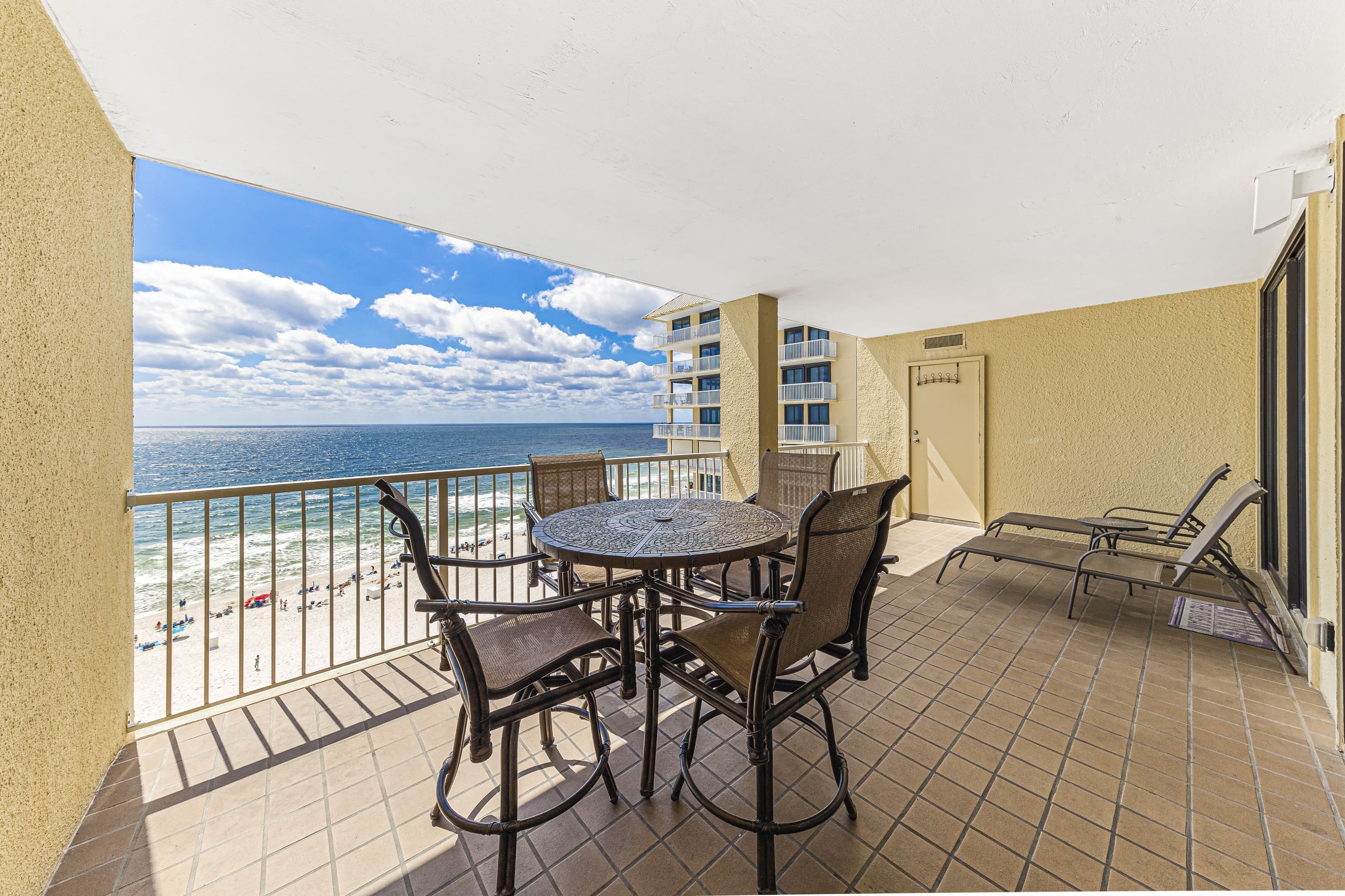 Un balcon avec vue sur la plage et l’océan, une table ronde avec des chaises, et un petit coin salon avec une table et des chaises.