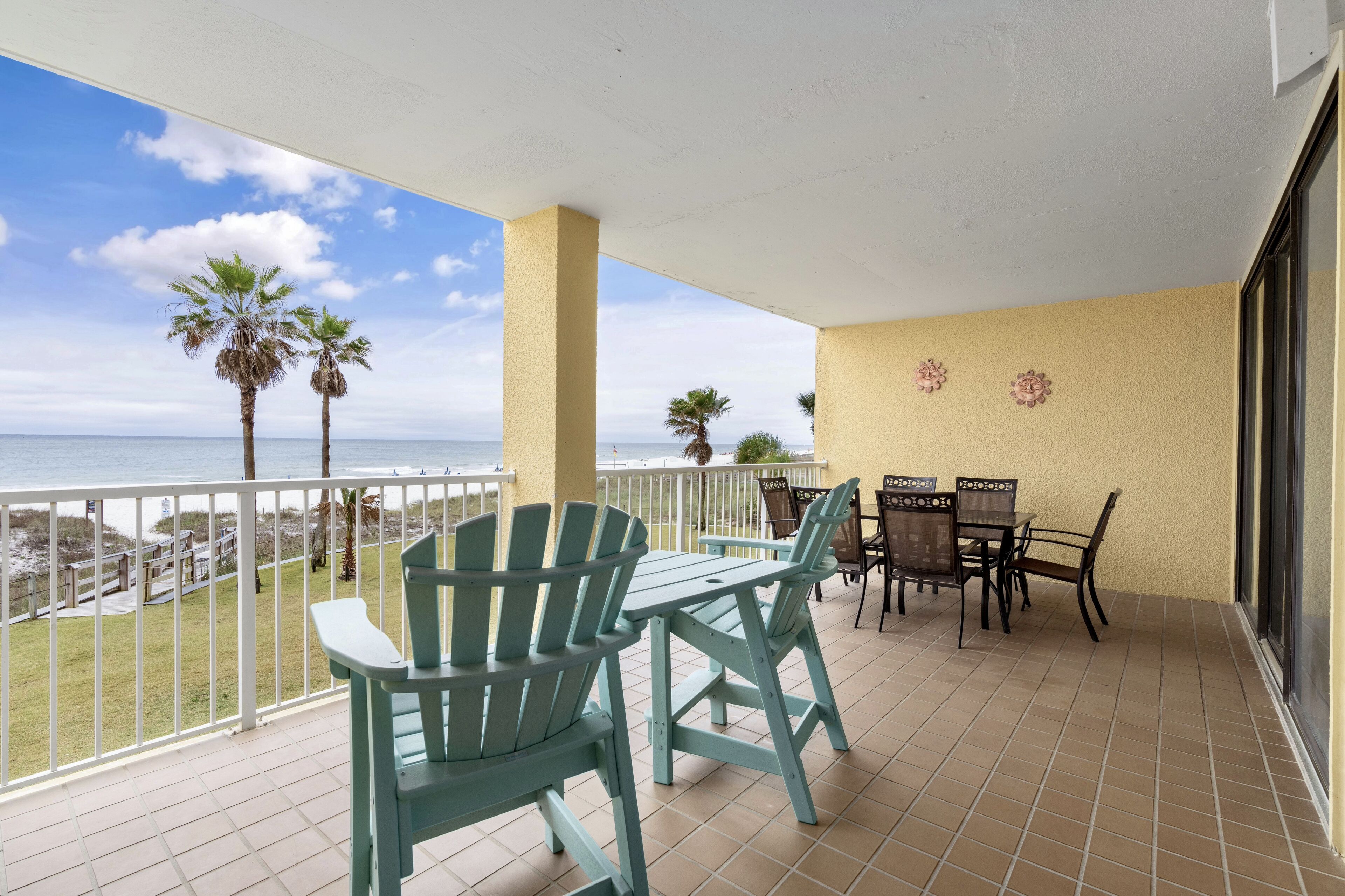 A balcony with a view of the beach, a table with chairs, and a small garden area.