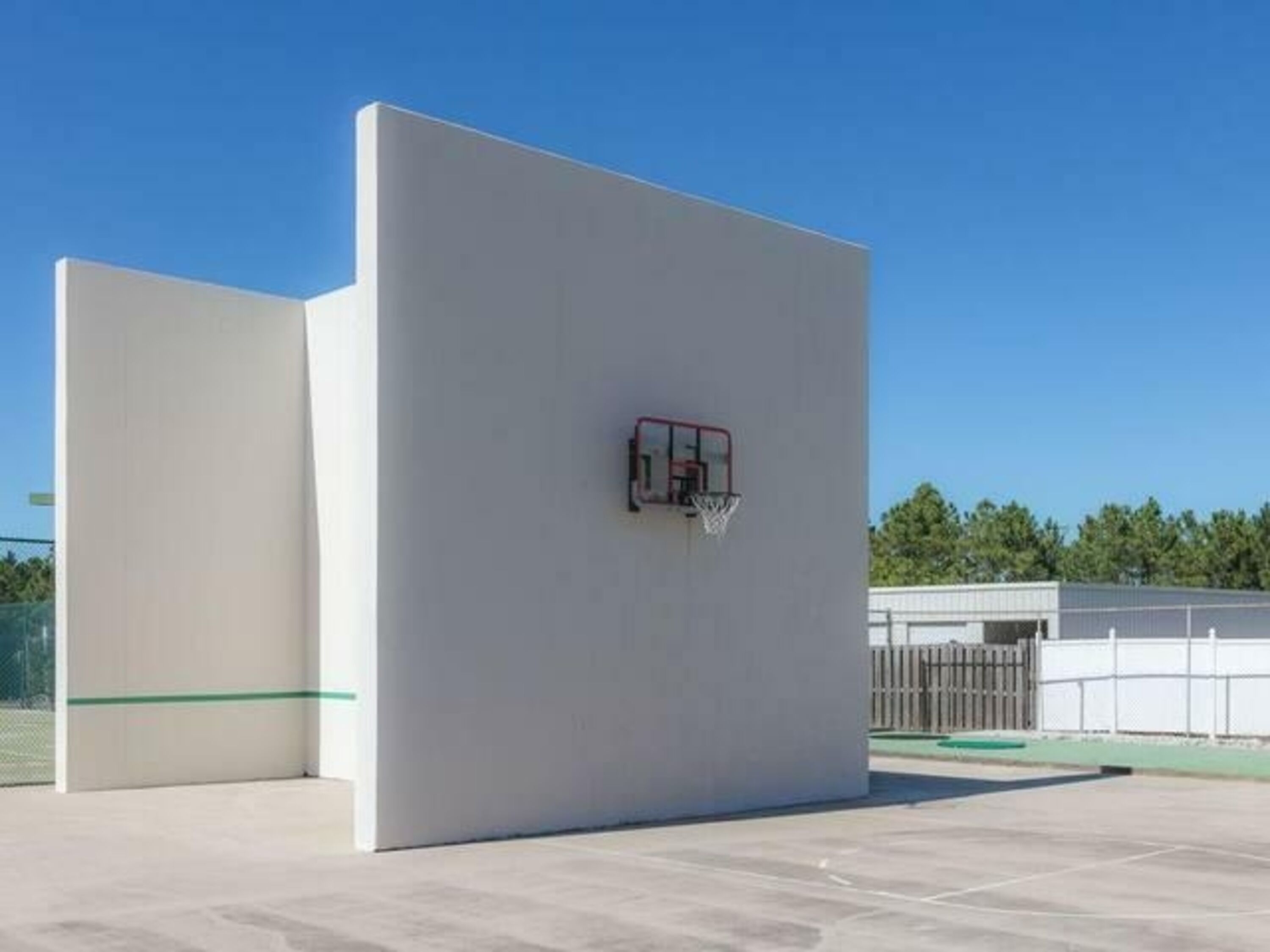 A basketball court with a hoop, a white wall, and a clear sky.