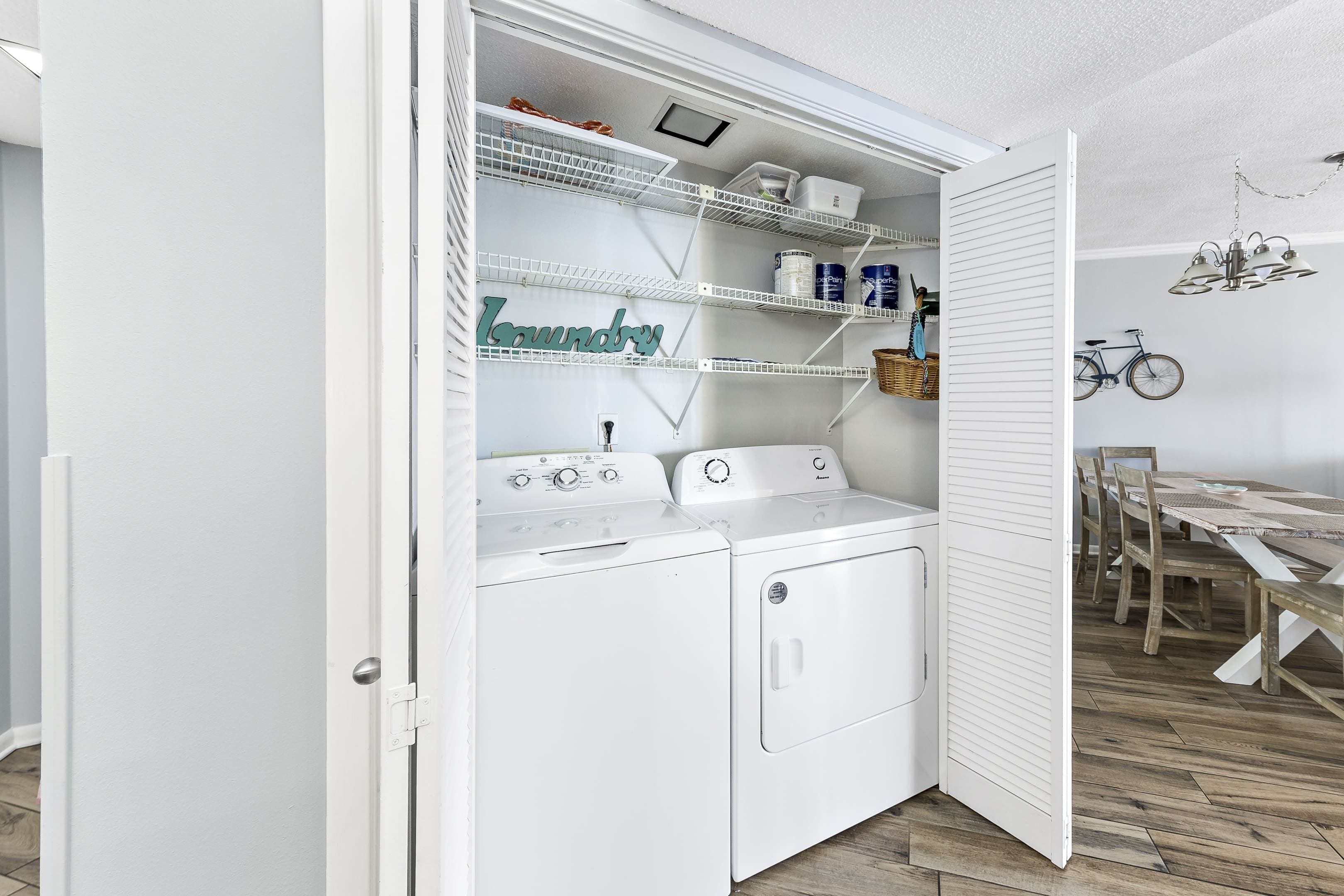 A laundry room with a built-in washer and dryer, shelves with laundry supplies, and a dining area with a wooden table and chairs.