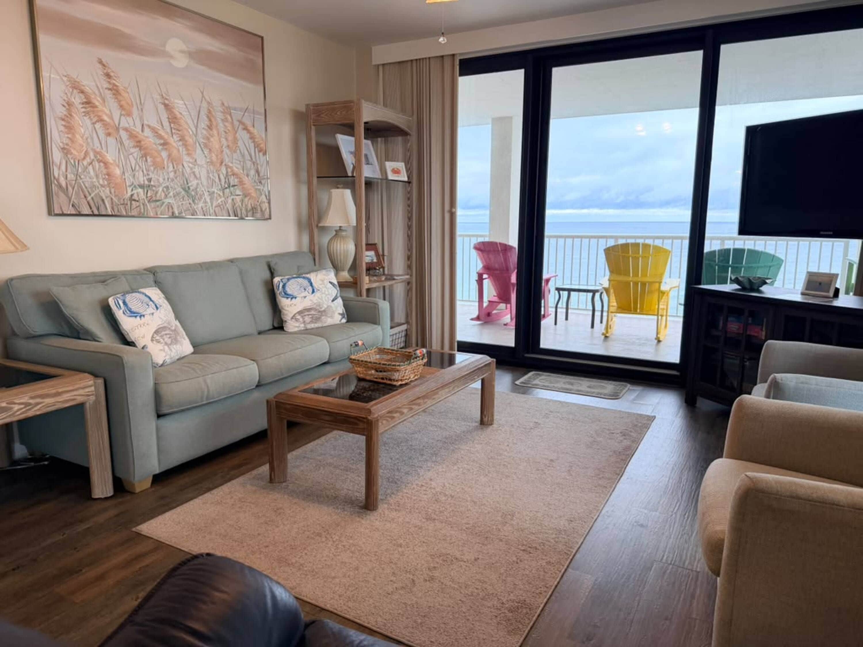 A living room with a sofa, a coffee table, and a view of the balcony with outdoor furniture.
