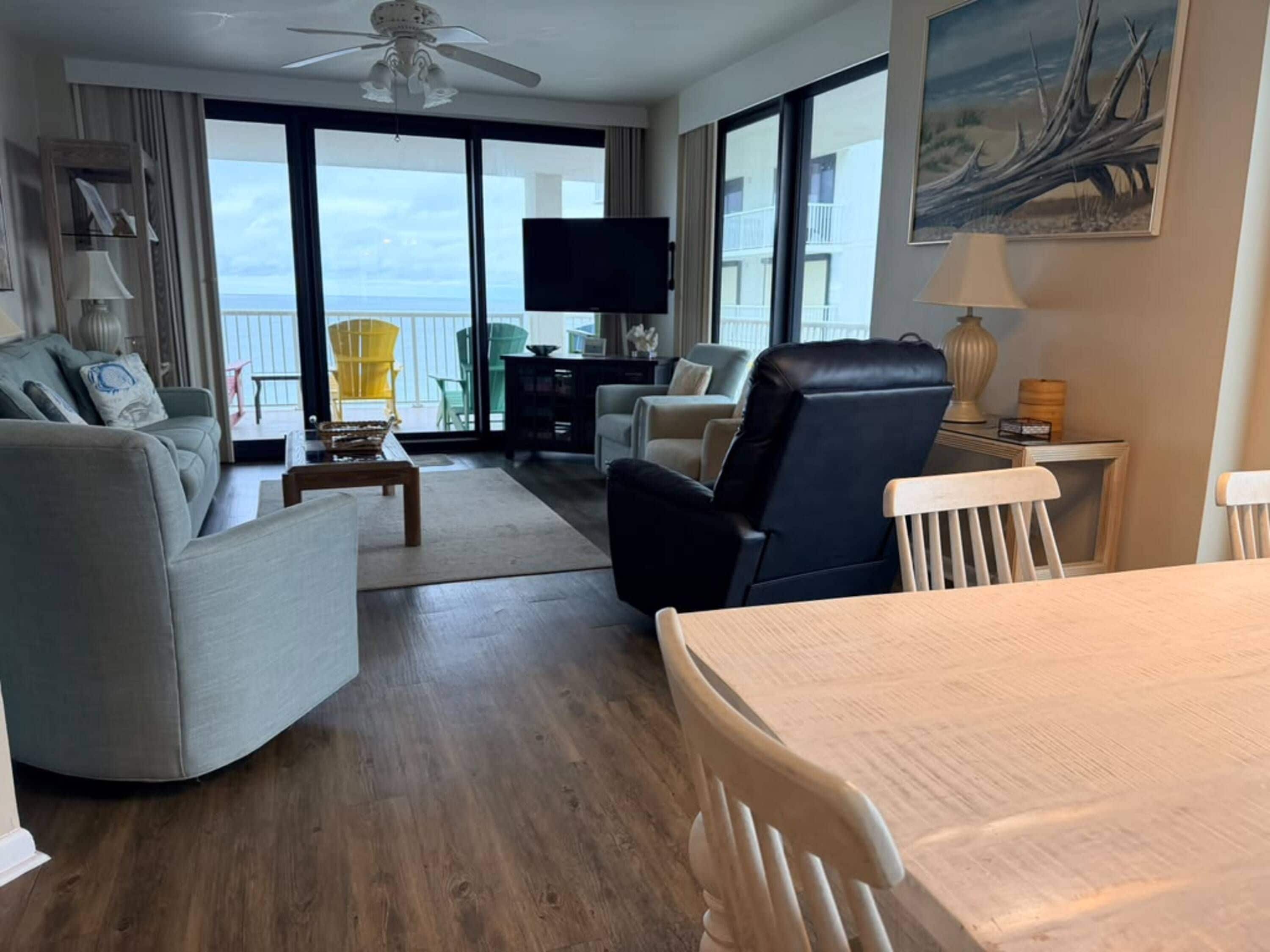 A modern hotel room with a sofa, armchairs, a dining table, and a TV.