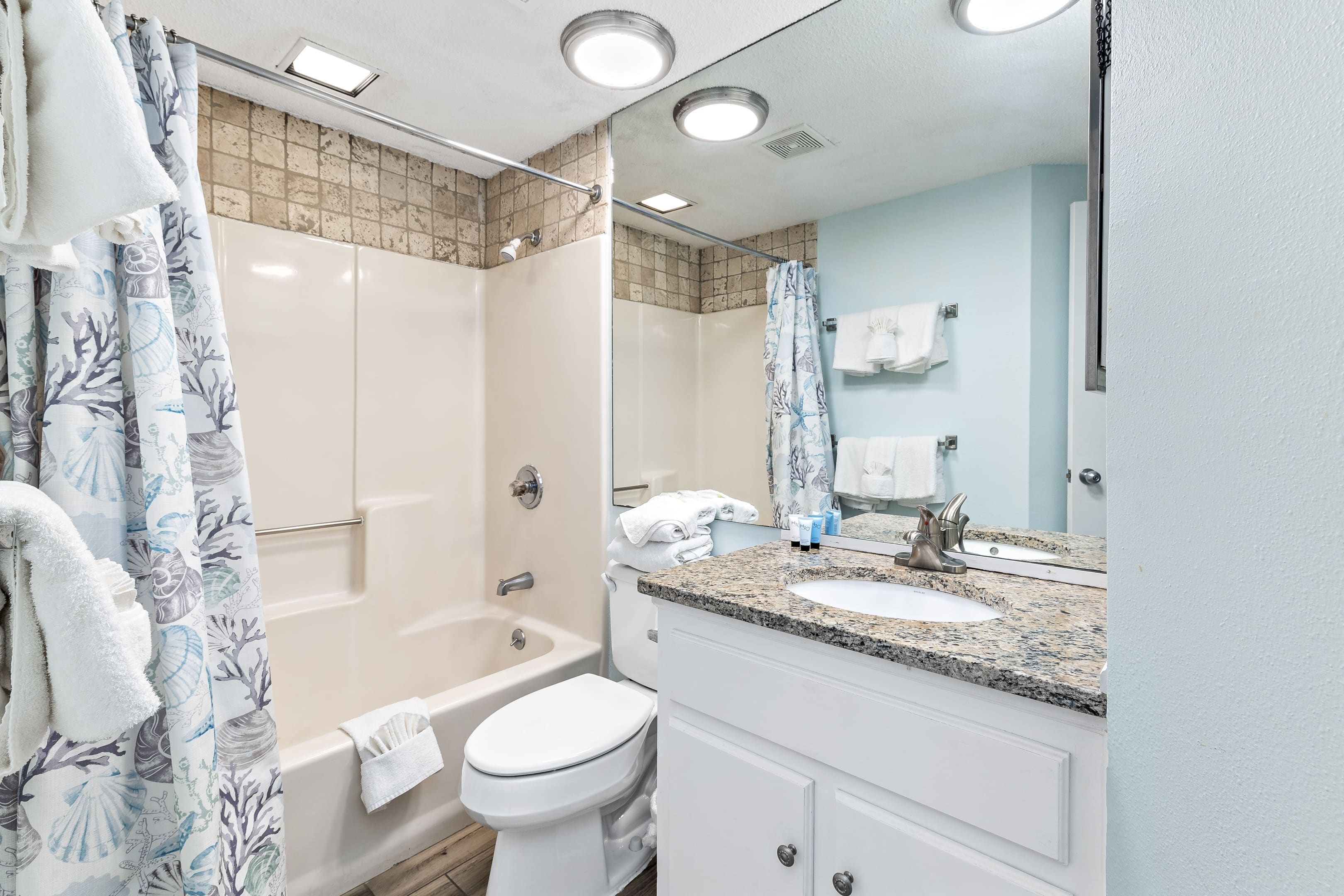 A bathroom with a shower, toilet, sink, and a mirror.