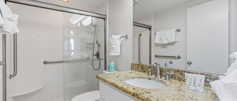 A modern bathroom with a glass shower enclosure, a white toilet, a granite countertop sink, and a large mirror.