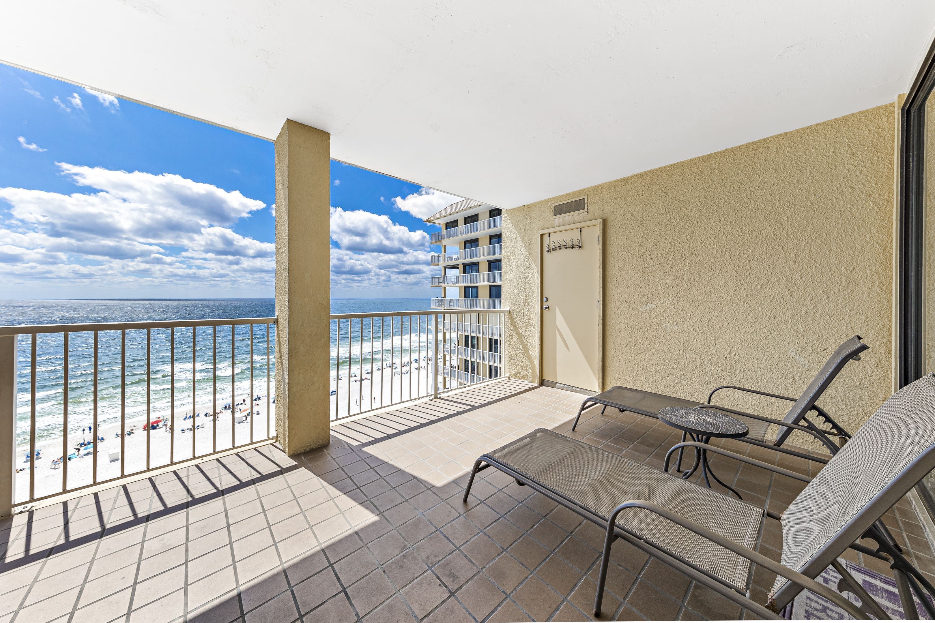A balcony with a view of the beach and ocean, a door, and two lounge chairs.