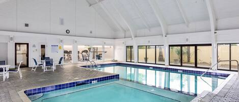An indoor swimming pool with a tiled edge, a covered roof, and a brick floor.