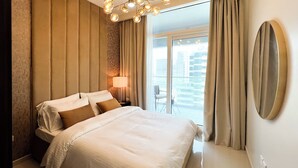 A hotel room with a large bed, a nightstand with a lamp, a view of the city through the window, and a balcony with a chair. - 1612 Damac Reva Residences (Dubai)