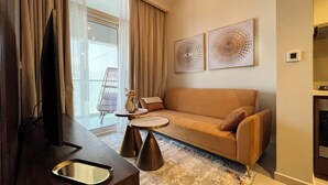 A modern living room with a sofa, a TV, and a coffee table. There are two artworks on the wall and a window with curtains. - 1612 Damac Reva Residences (Dubai)