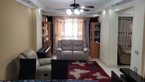 A living room with a ceiling fan, a sofa, a chair, a cabinet with glass doors, and a patterned rug. - Cozy 2-bedroom apartment with WiFi, AC in awesome Giza Governorate (Giza Governorate)