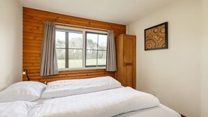 Une chambre à coucher avec une tête de lit en bois, une grande fenêtre avec des rideaux, un lit avec une literie blanche et un tableau encadré au mur.
