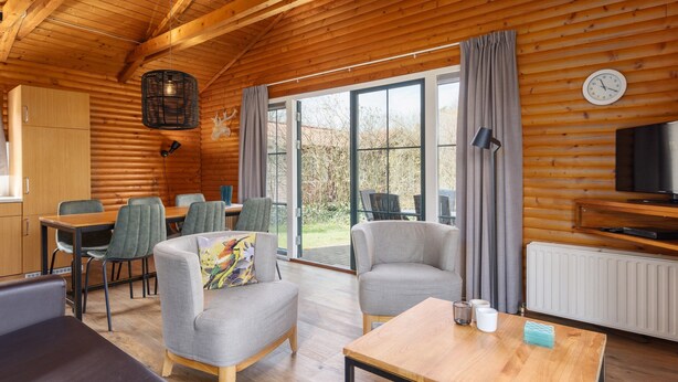 Un intérieur de chalet chaleureux comprenant un coin repas, deux fauteuils, un canapé, une table en bois et un téléviseur.