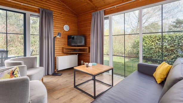 Una habitación acogedora de estilo cabaña con techo de madera, ventanas grandes, un sofá, una mesa y un televisor.