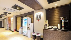 Ein Hotel-Empfangsbereich mit modernem Design, inklusive einer Rezeption, einem Kühlschrank, einer Verkaufsmaschine und einem Mülleimer.