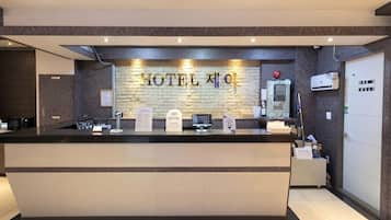 A hotel reception desk with a brick wall backdrop, a digital check-in kiosk, and a reception counter.
