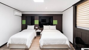 A hotel room with two beds, a desk, a chair, a TV, and a window with blinds.