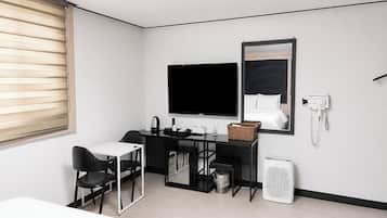 Une chambre d’hôtel comprenant un lit, un bureau avec une chaise, une télévision, un miroir, un téléphone et une poubelle.