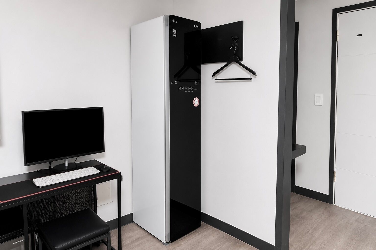 Quarto de hotel com escrivaninha, televisão de tela plana, guarda-roupa preto e uma porta.