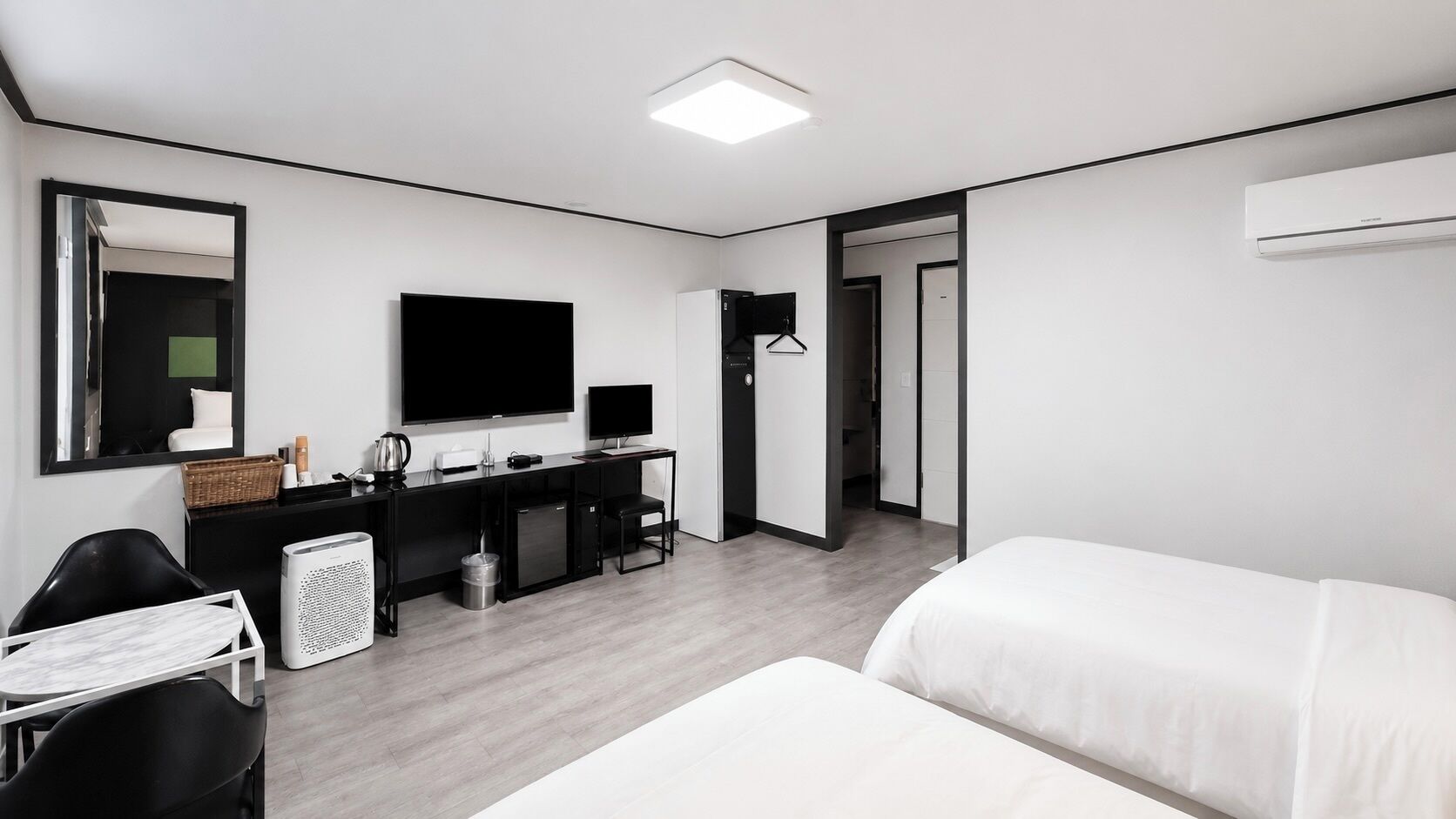 Quarto de hotel moderno com cama, escrivaninha com computador, televisão e espelho.