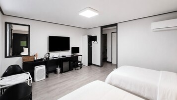 Quarto de hotel moderno com cama, escrivaninha com computador, televisão e espelho.