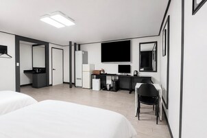 Quarto de hotel com duas camas, uma mesa com computador, frigorífico, lixeira e espelho.