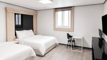 Habitación de hotel con dos camas, un escritorio, una silla, un televisor y una ventana.