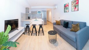 Ein modernes Wohnzimmer mit einem grauen Sofa, schwarzen Hocker, einem Fernseher und einem kleinen runden Tisch.