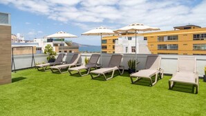 Eine Dachterrasse mit Kunstgrasanlage, Liegestühlen und Sonnenschirmen.