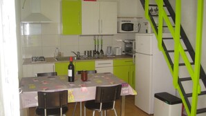 Une cuisine de taille réduite comprenant une table à manger, des chaises, une bouteille de vin et les appareils électroménagers de base.