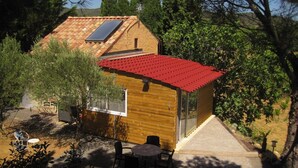 Une petite cabane en bois avec un toit rouge, un panneau solaire et un espace patio avec des sièges d’extérieur.