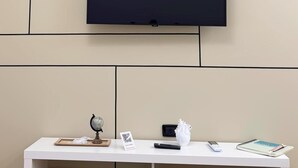 Un téléviseur à écran plat fixé au mur, au-dessus d’un meuble télé blanc sur lequel se trouvent un globe terrestre, une télécommande, un petit objet blanc et un carnet.