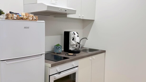 Une cuisine moderne avec des meubles blancs, un four encastré, une machine à café et un évier.