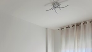 Une chambre à coucher au style minimaliste, avec un lit blanc, une table de chevet et un ventilateur de plafond.