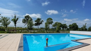 A rectangular outdoor swimming pool with a clear blue water surface, surrounded by a tiled deck and a low fence. - Charming Sauna Home Near Alkmaar (West-Graftdijk)