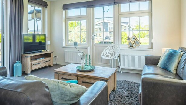 A living room with a sofa, a coffee table, a TV, and a chair. - Charming Sauna Home Near Alkmaar (West-Graftdijk)