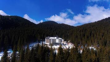 A multi-story building surrounded by dense forest, with snow on the ground and a clear blue sky.