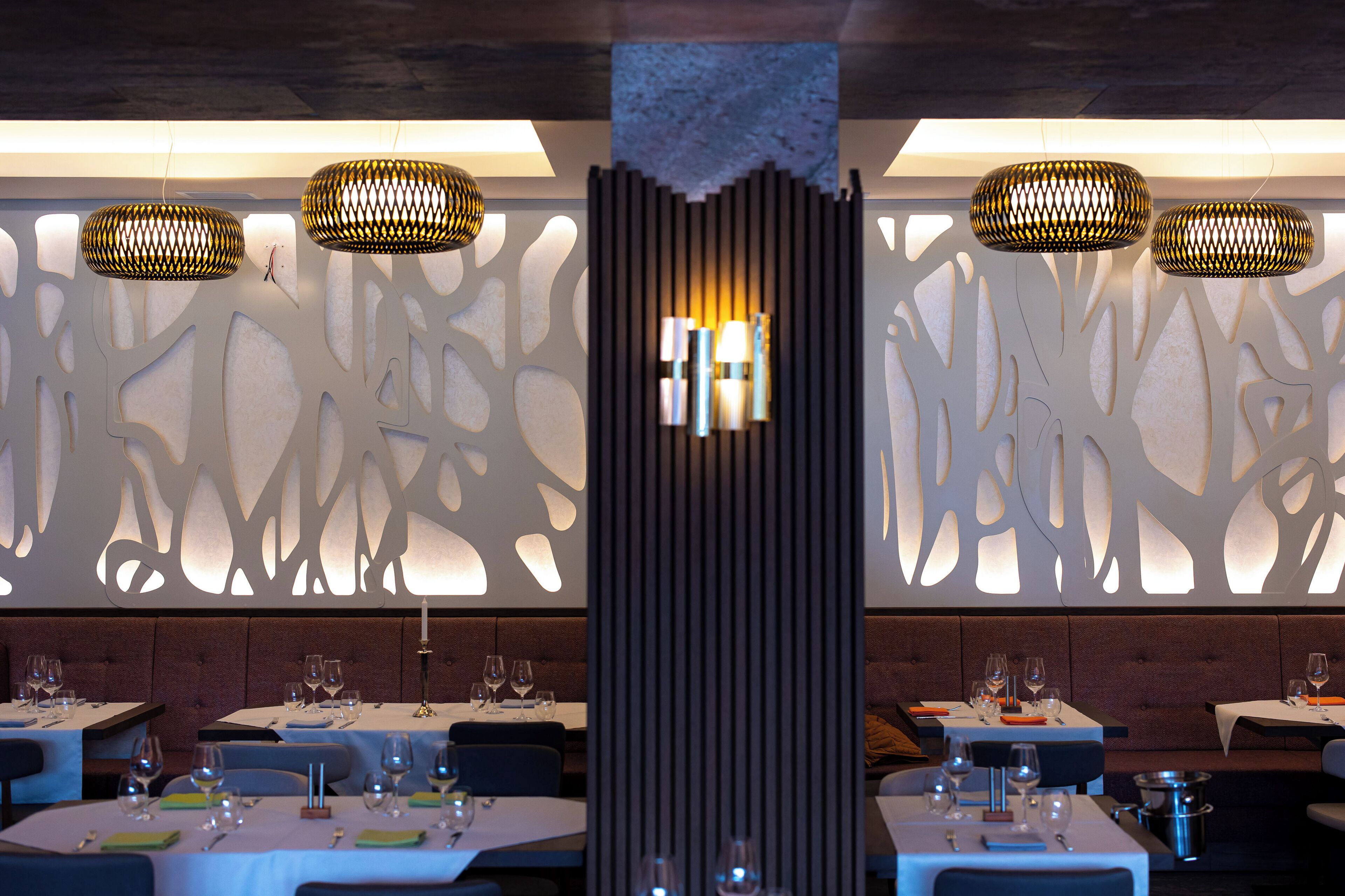 A restaurant interior with tables set for dining, decorative wall panels, and hanging pendant lights.