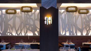 A restaurant interior with tables set for dining, decorative wall panels, and hanging pendant lights.