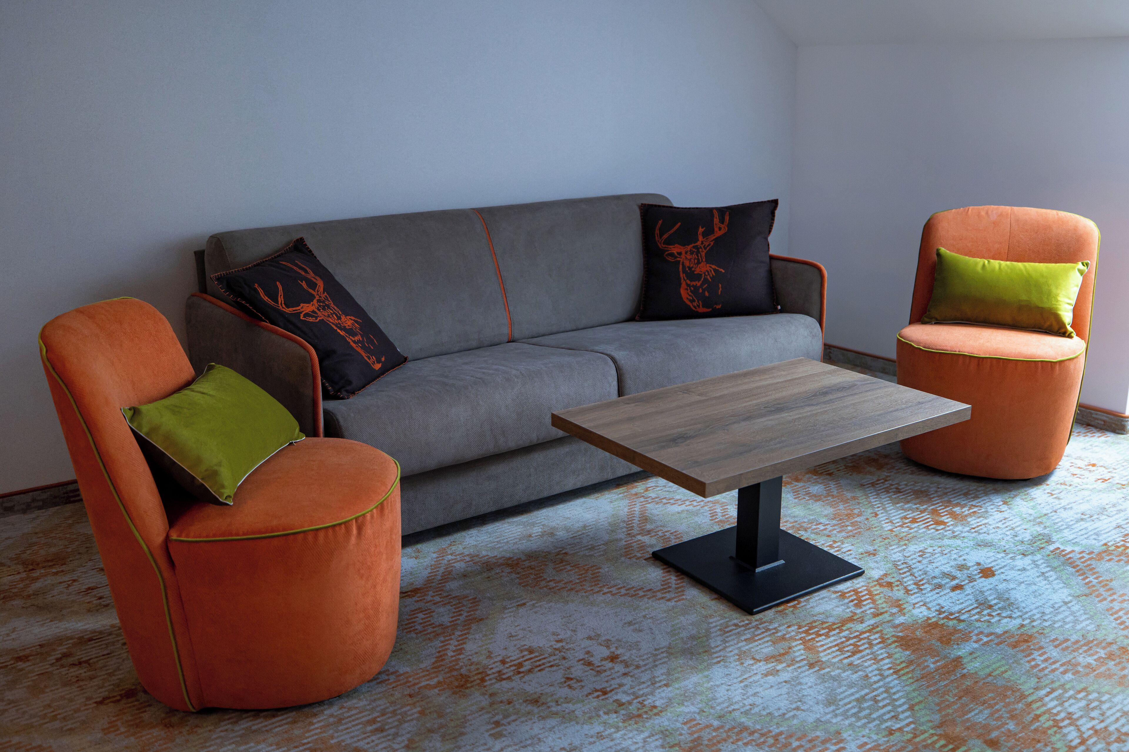 A living room with a grey sofa, two orange armchairs, and a wooden coffee table.