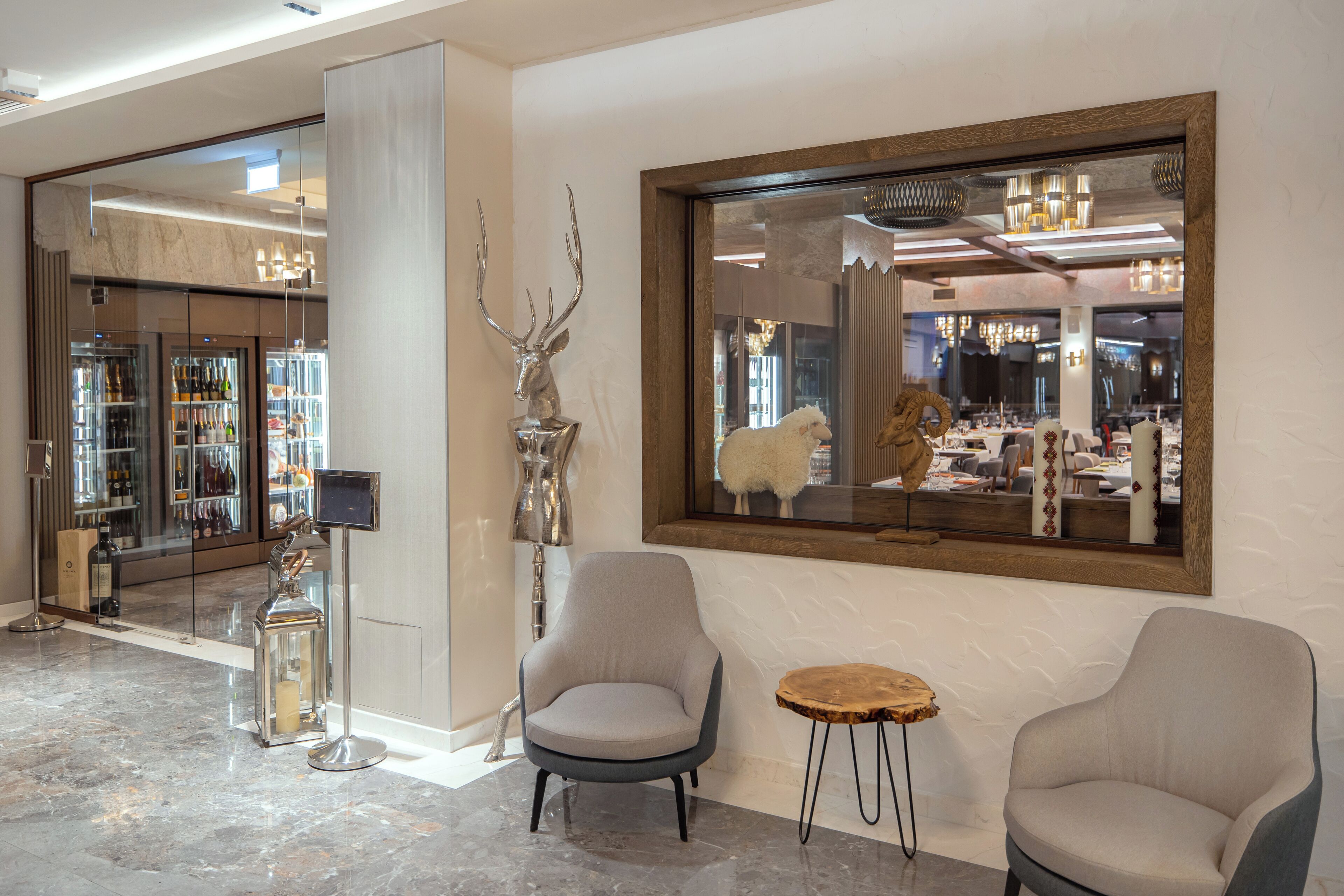 A lobby with two armchairs, a small round table, a large mirror, and a glass display case with bottles.