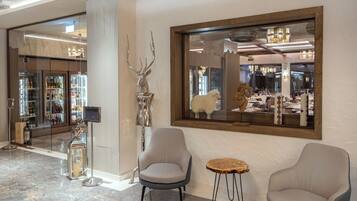 A lobby with two armchairs, a small round table, a large mirror, and a glass display case with bottles.