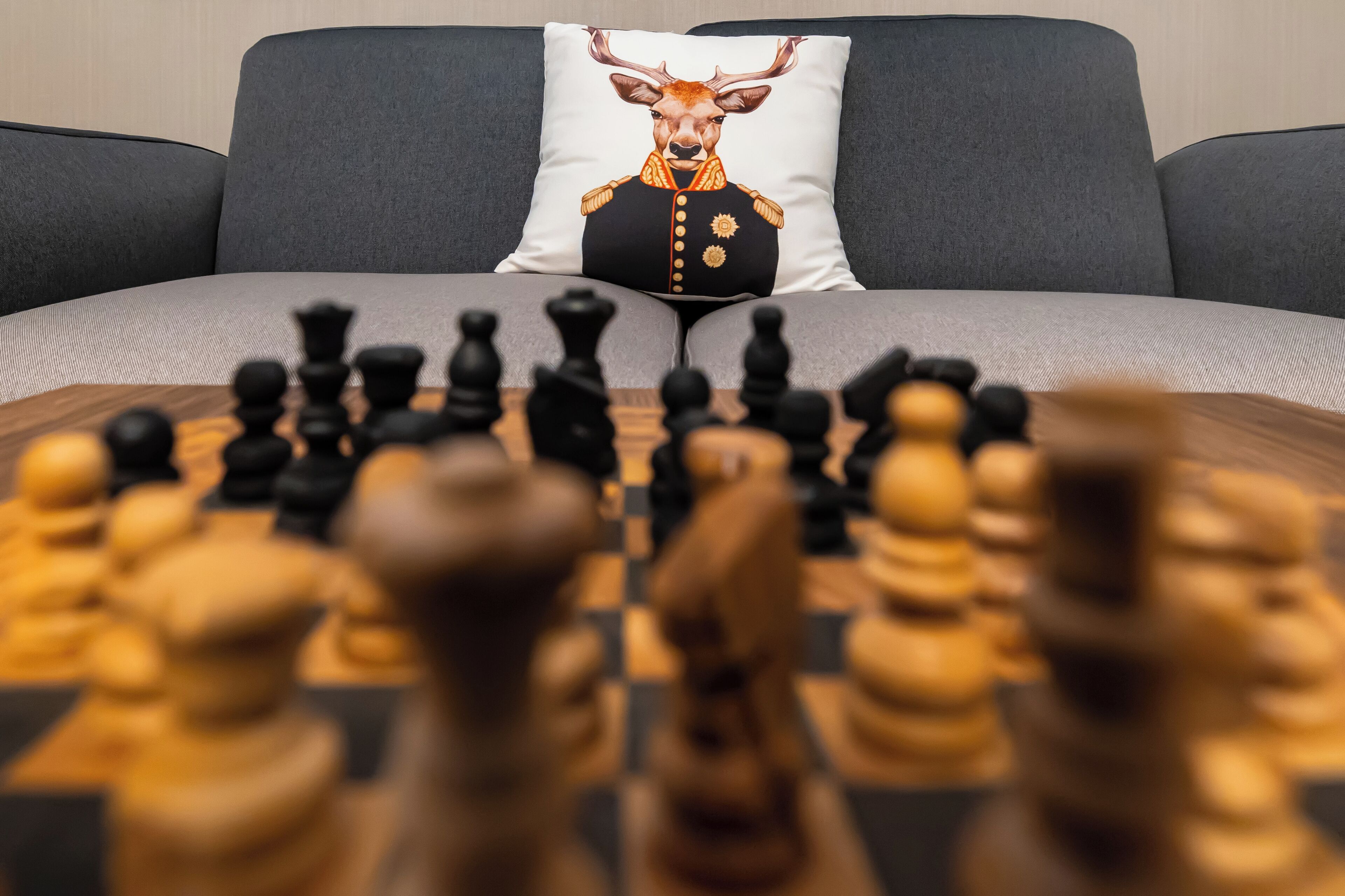 A chessboard on a table with a sofa and a pillow with a deer design in the background.