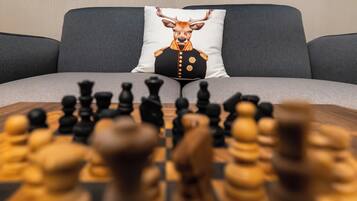 A chessboard on a table with a sofa and a pillow with a deer design in the background.